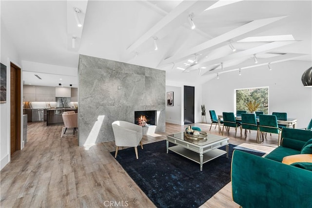 living room featuring vaulted ceiling with beams, light wood-style floors, and a premium fireplace