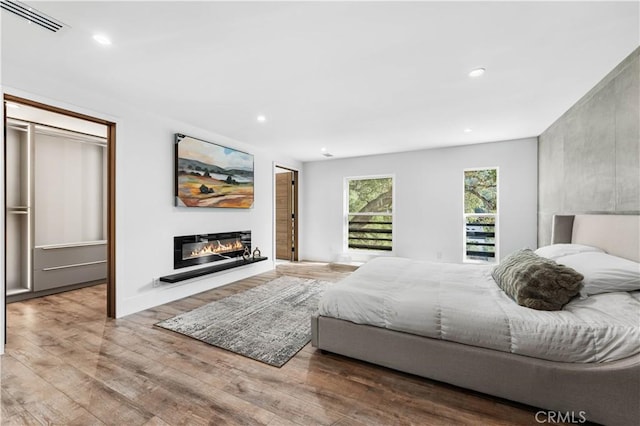 bedroom with wood finished floors, a glass covered fireplace, visible vents, and recessed lighting