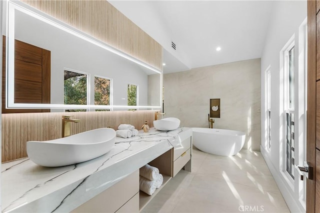 bathroom with double vanity, a freestanding tub, a sink, and recessed lighting