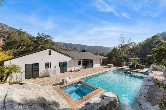 view of pool featuring a patio, a pool with connected hot tub, a mountain view, fence, and a pergola