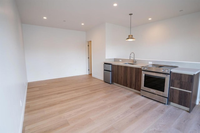 kitchen featuring stainless steel appliances, hanging light fixtures, sink, and light hardwood / wood-style flooring