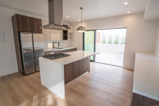 kitchen with sink, appliances with stainless steel finishes, pendant lighting, island exhaust hood, and light hardwood / wood-style floors