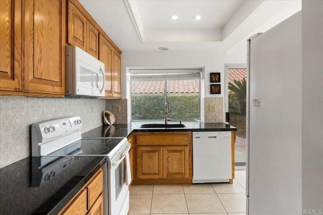 kitchen with sink, decorative backsplash, light tile patterned floors, a tray ceiling, and white appliances