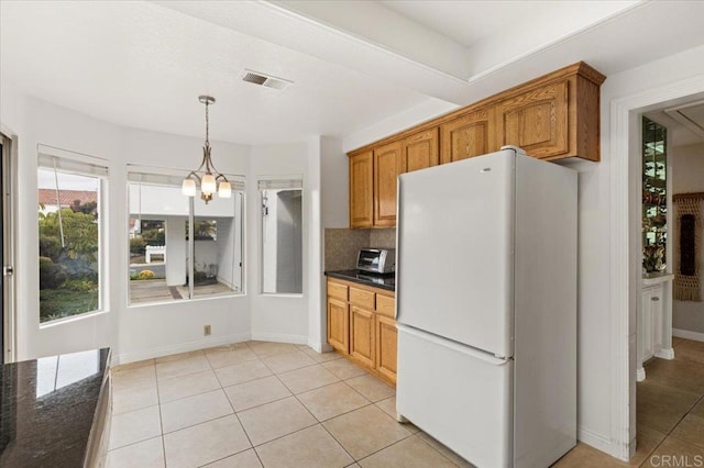 kitchen featuring light tile patterned floors, backsplash, white refrigerator, decorative light fixtures, and dark stone counters