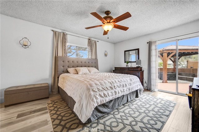 bedroom featuring a ceiling fan, access to outside, light wood-style floors, and a textured ceiling