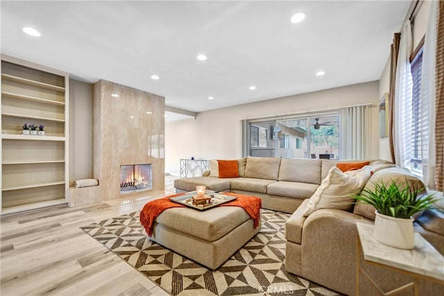 living room featuring light wood-style flooring, recessed lighting, a premium fireplace, and built in shelves