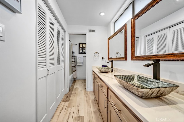 bathroom featuring a sink, visible vents, double vanity, and wood finished floors