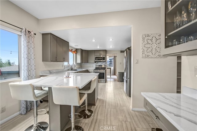 kitchen featuring light stone countertops, a peninsula, appliances with stainless steel finishes, a sink, and baseboards