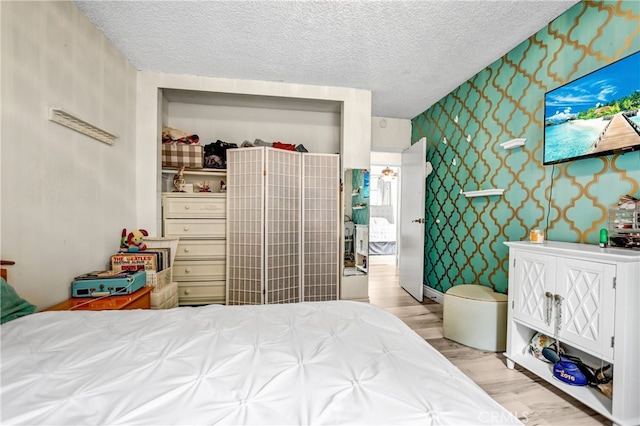 bedroom featuring a textured ceiling, light wood finished floors, and wallpapered walls