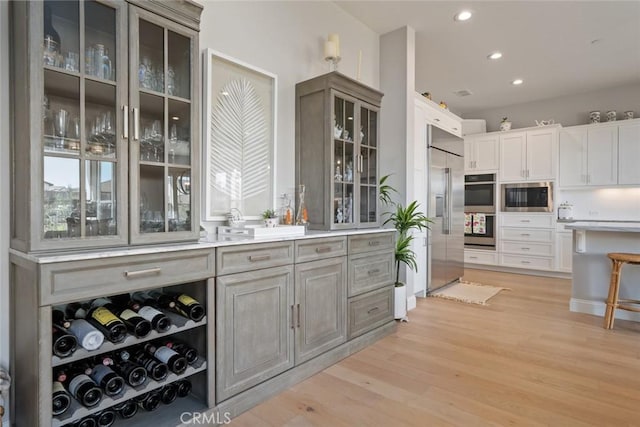 bar featuring built in appliances, light hardwood / wood-style floors, white cabinets, and gray cabinetry