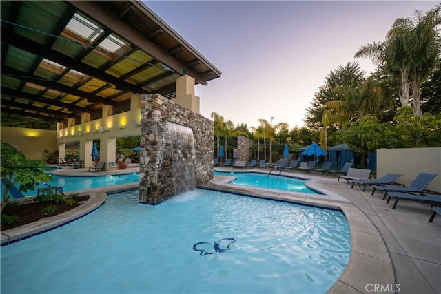 pool at dusk with pool water feature and a jacuzzi