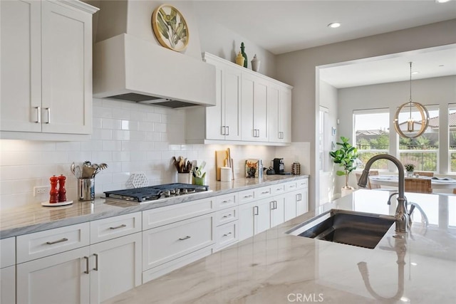 kitchen featuring sink, white cabinetry, light stone countertops, custom range hood, and decorative light fixtures