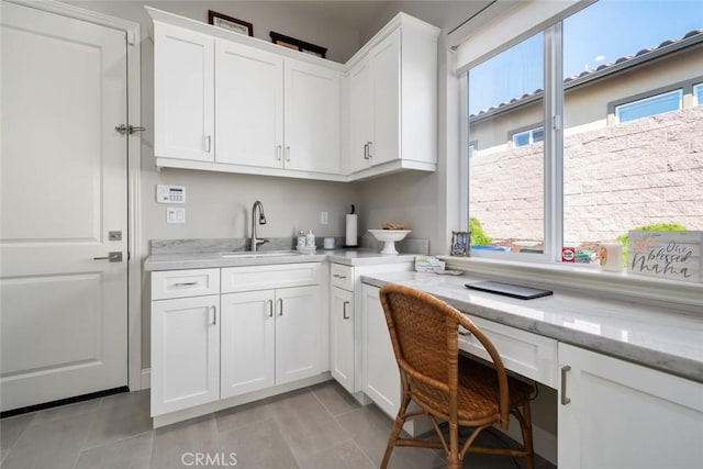 kitchen featuring sink, built in desk, light tile patterned floors, light stone countertops, and white cabinets