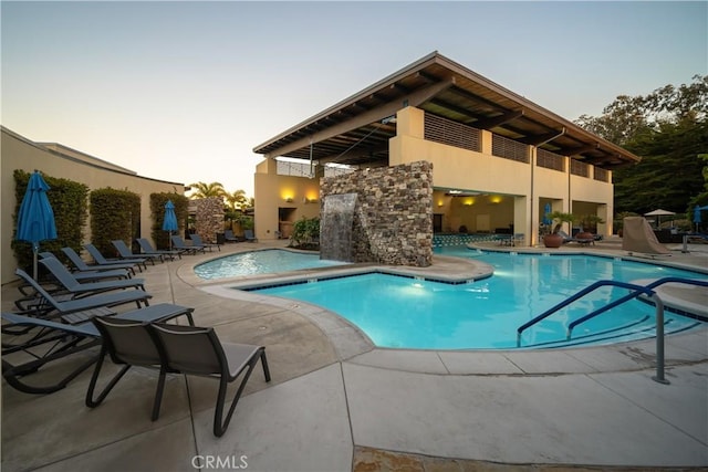 pool at dusk with pool water feature, a jacuzzi, and a patio area