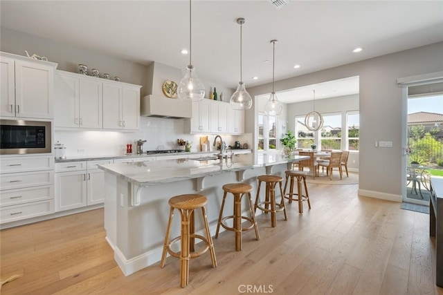 kitchen with pendant lighting, sink, white cabinetry, a center island with sink, and built in microwave