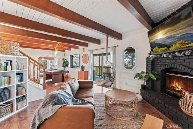 sitting room with a brick fireplace, beam ceiling, stairway, and wood finished floors