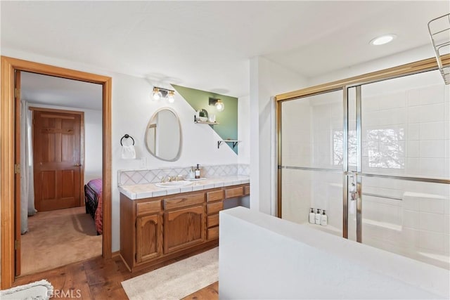 full bath featuring a tile shower, vanity, and wood finished floors