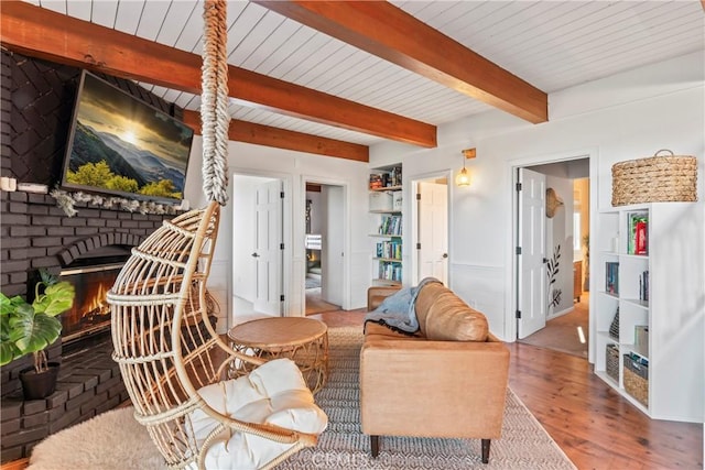 living room featuring beam ceiling, a fireplace, and wood finished floors