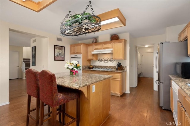 kitchen featuring light stone counters, a kitchen island, wood-type flooring, and appliances with stainless steel finishes