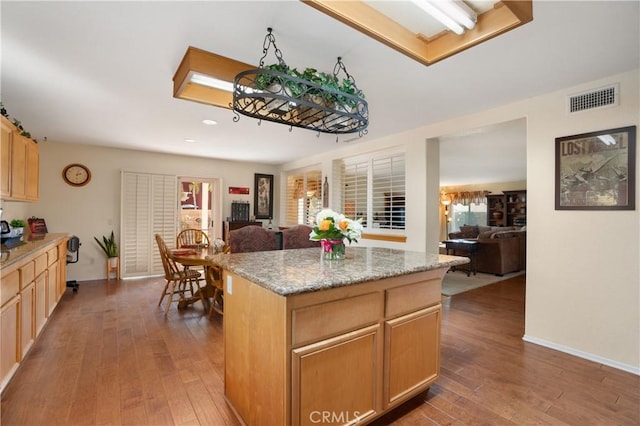 kitchen featuring hardwood / wood-style flooring, light brown cabinetry, a center island, and light stone countertops