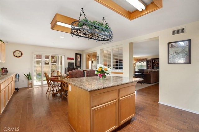 kitchen with hardwood / wood-style flooring, a center island, light brown cabinetry, and light stone counters