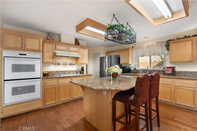 kitchen featuring white appliances, wood-type flooring, a center island, and a breakfast bar area