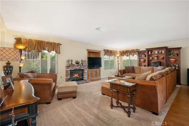 living room featuring a brick fireplace, light hardwood / wood-style flooring, and a healthy amount of sunlight