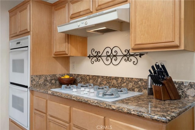 kitchen with dark stone countertops, white appliances, and light brown cabinets