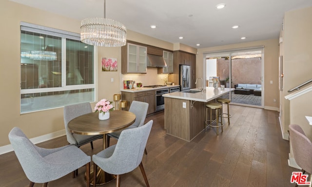 kitchen with sink, appliances with stainless steel finishes, a kitchen breakfast bar, dark hardwood / wood-style floors, and a center island with sink