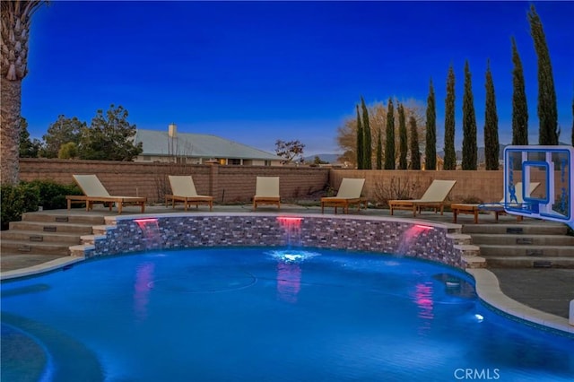 pool at dusk with a patio area and pool water feature