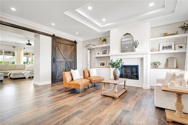 living room featuring crown molding, hardwood / wood-style flooring, a barn door, and a raised ceiling