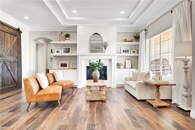 sitting room featuring dark hardwood / wood-style floors, a tray ceiling, ornamental molding, a large fireplace, and a barn door