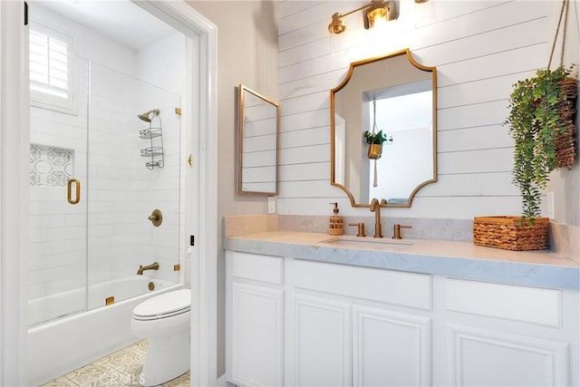 full bathroom featuring wooden walls, vanity, toilet, and combined bath / shower with glass door