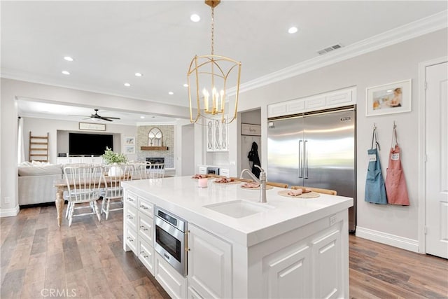 kitchen with hanging light fixtures, white cabinetry, sink, and a kitchen island with sink