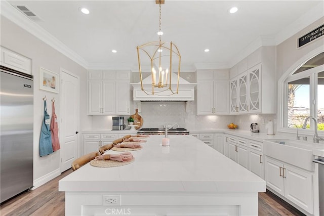 kitchen with appliances with stainless steel finishes, decorative light fixtures, sink, white cabinets, and a center island with sink