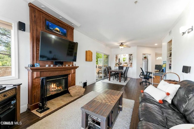 living area with baseboards, visible vents, a fireplace with flush hearth, dark wood-style flooring, and crown molding