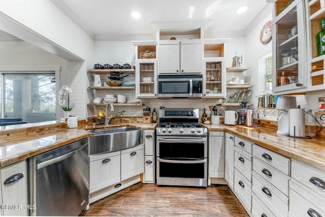 kitchen with a sink, stainless steel appliances, open shelves, and crown molding