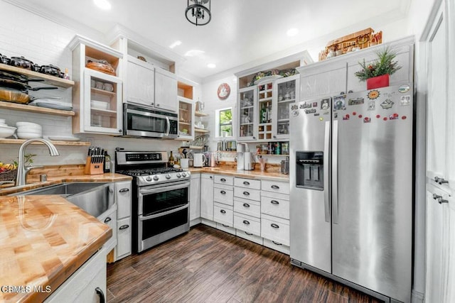 kitchen featuring stainless steel appliances, a sink, open shelves, dark wood finished floors, and crown molding