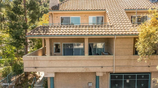 back of house featuring a chimney, a tile roof, and a balcony
