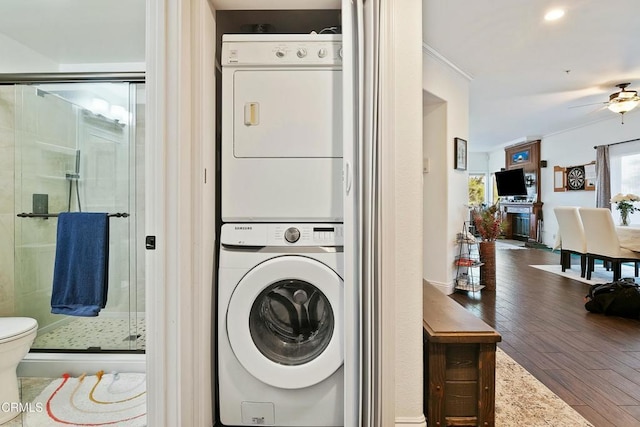 clothes washing area with stacked washing maching and dryer, a ceiling fan, and wood finished floors
