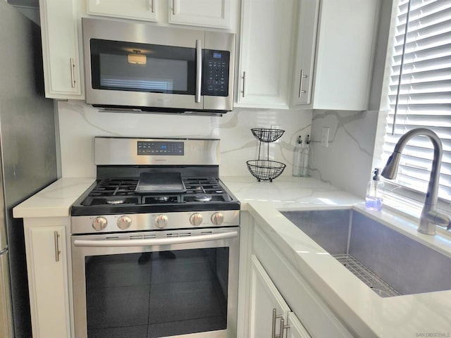 kitchen featuring stainless steel appliances, white cabinetry, light stone countertops, and sink