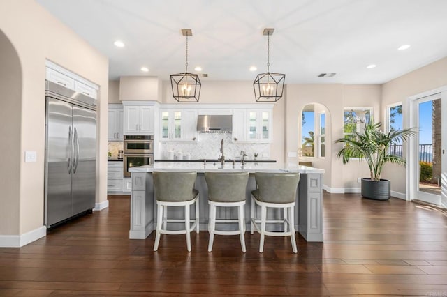 kitchen with stainless steel appliances, wall chimney exhaust hood, light countertops, and backsplash