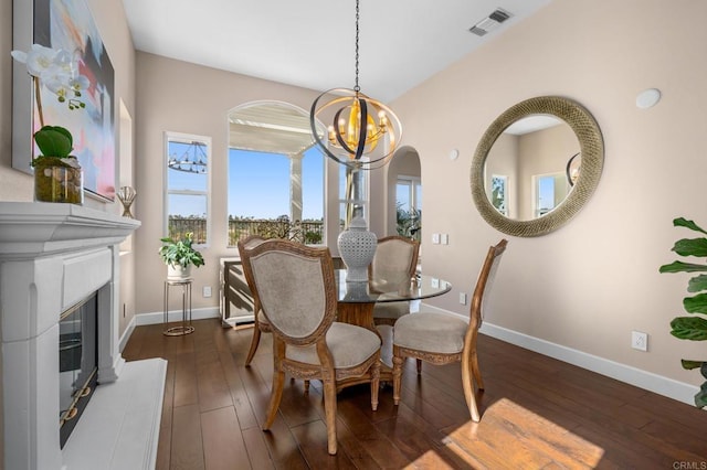 dining area featuring a chandelier, dark wood-type flooring, visible vents, baseboards, and a glass covered fireplace