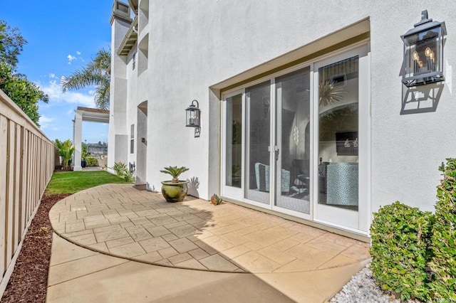 view of exterior entry with a patio area, fence, and stucco siding