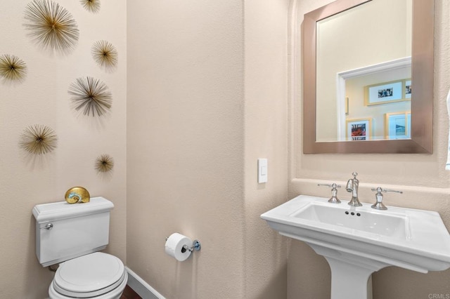 half bathroom featuring toilet, baseboards, and a sink