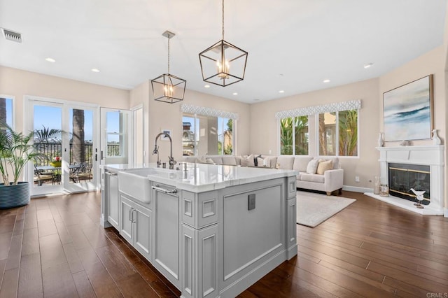 kitchen featuring a glass covered fireplace, a sink, visible vents, open floor plan, and dark wood finished floors