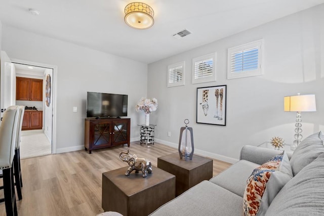 living room with light wood-type flooring, visible vents, and baseboards