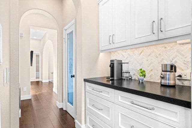 bar with baseboards, arched walkways, dark wood-style flooring, and backsplash