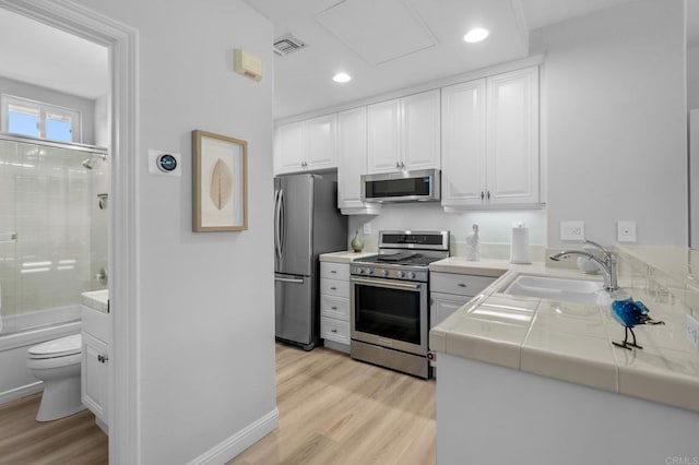 kitchen with a sink, appliances with stainless steel finishes, white cabinetry, and visible vents