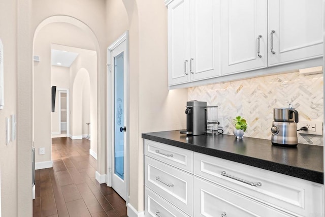 interior space with dark wood-type flooring, arched walkways, decorative backsplash, and baseboards